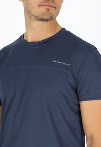 Marineblå t-shirt med korte ærmer, der har et struktureret stof, et subtilt logo ved skulderen og en rund halsudskæring. Glat, atletisk pasform.