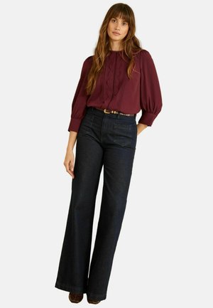 Burgundy blouse with puffy sleeves and scalloped details paired with dark blue wide-leg jeans, featuring pockets and a brown belt.