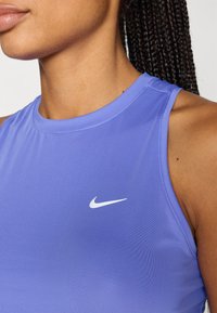 Μωβ αμάνικη αθλητική μπλούζα από απαλό ύφασμα με στρογγυλή λαιμόκοψη και λευκό λογότυπο Nike Swoosh στην αριστερή πλευρά του στήθους.