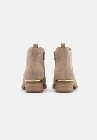 Stivaletti alla caviglia in suede beige con tacco decorato in oro, caratterizzati da un design elegante e da una chiusura con zip sul retro per un indossamento facile.