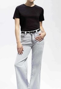 T-shirt en coton noir à manches courtes, associé à un jean en denim gris clair taille haute. Présente une ceinture noire avec des accents en métal argenté.
