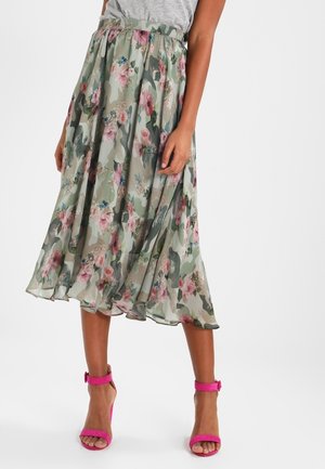 Gonna midi con stampa camouflage floreale verde, beige e rosa, indossata con top grigio e sandali con tacco alto e cinturino alla caviglia rosa acceso.