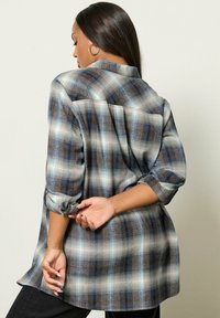 Långärmad rutigt skorta i nyanser av blått och brunt, med en avslappnad passform, rullade ärmar och en rundad nederkant.