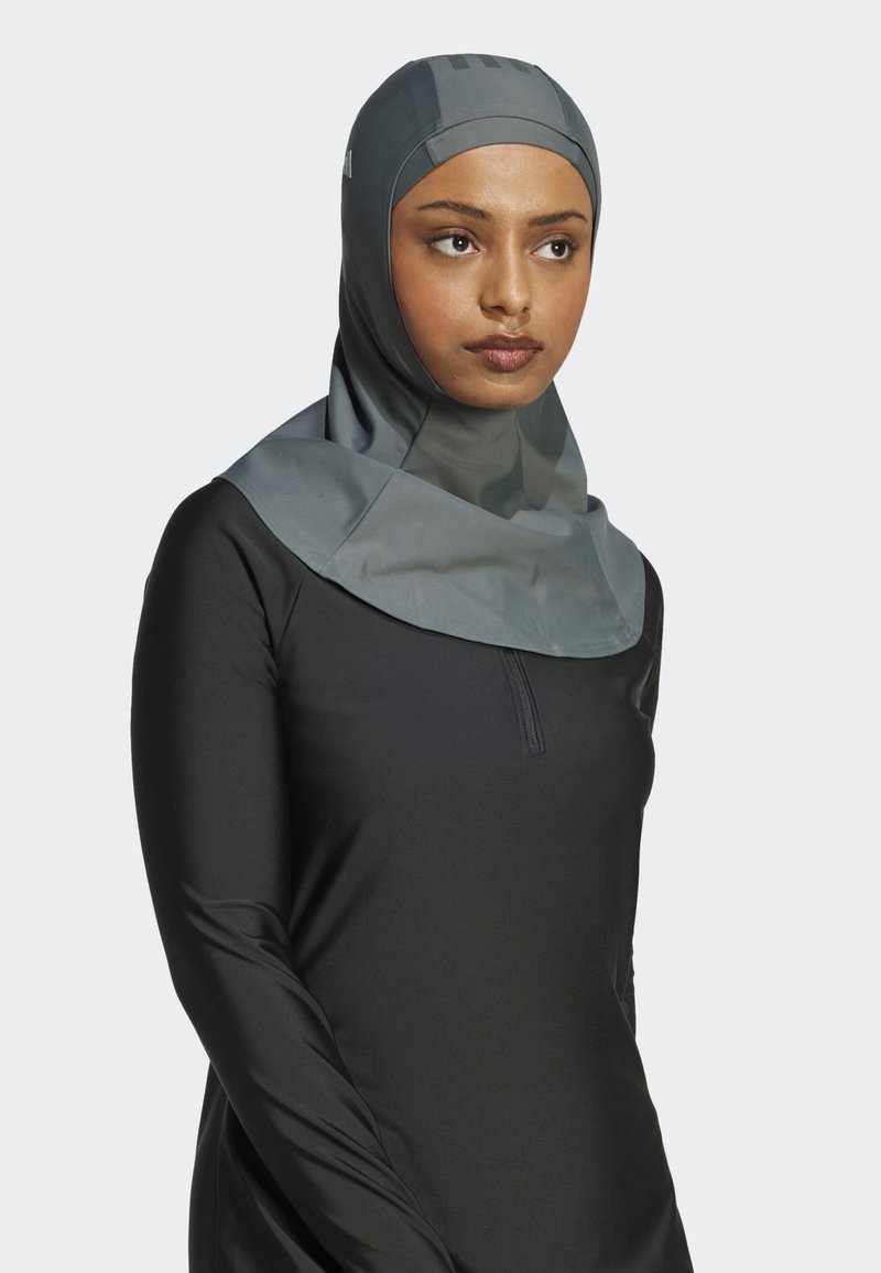 Grauer Sportshijab aus leichtem, atmungsaktivem Material, mit hohem Kragen und glatter Textur. Trägt einen schwarzen Langarm-Top.