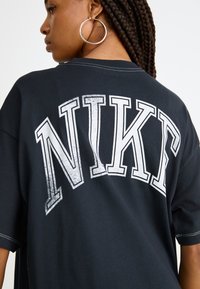 Black cotton t-shirt with oversized fit, featuring white distressed "NIKE" text on the back, and short sleeves.