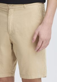 Shorts en velours côtelé beige avec une texture lisse, poches avant et fermeture à bouton. Les finitions de l'ourlet sont droites et nettes.