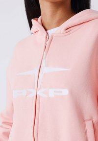 Lichtroze zip-up hoodie met een wit logo, voorzien van een trekkoordkap, zachte textuur en voorzakken.
