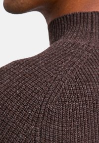 Brauner Strickpullover mit hohem Kragen, einem strukturierten Muster und gerippten Details am Halsausschnitt und an den Schultern.