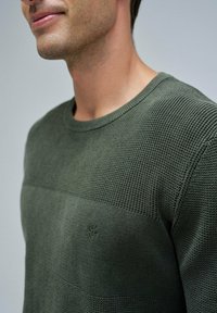Olive green knit sweater with textured horizontal stripes, round neckline, and small embroidered logo on the lower left side.