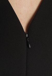 Tela de vestido negra con superficie texturizada y escote en V, que cuenta con un cierre de cremallera negra en el centro.