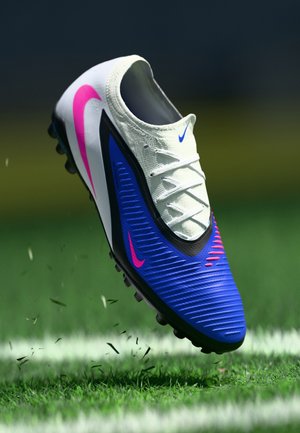 Nike voetbalschoen met een wit-blauw bovenwerk met roze accenten, gestructureerd ontwerp, zwarte zool met noppen en witte veters.