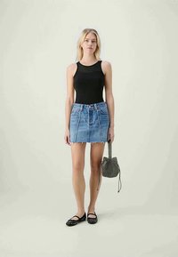 Black fitted tank top, denim mini skirt with frayed hem, black flats with studs, and a small patterned handbag. Light background.