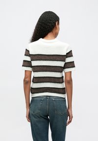 Kurzärmeliger Pullover in Weiß, Braun und Schwarz gestreift. Weiches Material mit tailliertem Design, geripptem Kragen und Saum. Sichtbare Denim-Jeans.