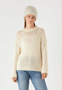 Lichtbeige gebreide trui met een brede halslijn, verlaagde schouders en lange mouwen. Draagt een bijpassende ribgebreide beanie. Casual pasvorm.