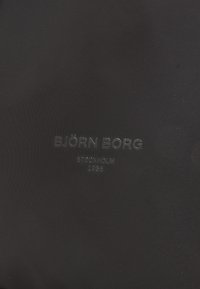 Melnas audums ar strukturētu apdari, uz kura ir reljefā tekst�ā izceltas frāzes: "BJÖRN BORG," "STOCKHOLM" un "1984" subtilā pelēkā tonī.