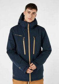 Giacca impermeabile blu navy con un ampio cappuccio, dettagli in beige per la zip e le tasche, area delle spalle texturizzata e polsini regolabili.