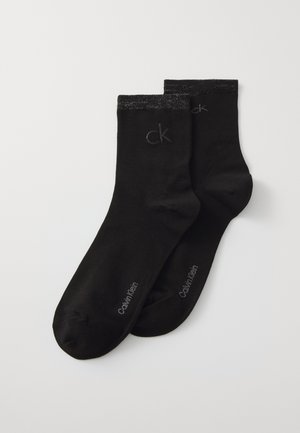 Black cotton socks with a smooth texture. Features a contrasting dark band at the top and printed "Calvin Klein" and "ck" logos.