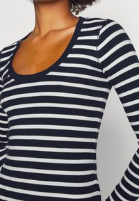 Marinblå och vit randig långärmad topp med rundad halsringning, tillverkad av ribbat tyg med konsekventa horisontella mönster.