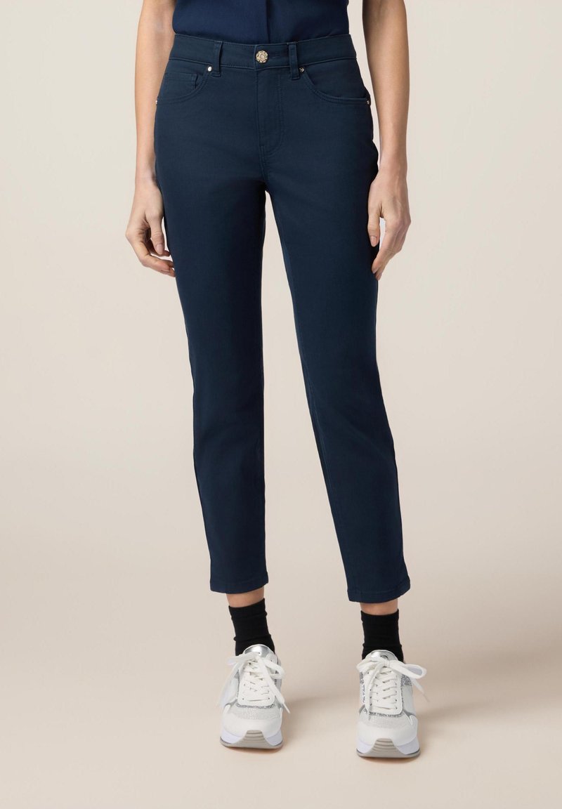 Navyblauwe enkellange broeken met een aangesloten design, voorzien van voorzakken en een knoopsluiting. Gepaard met witte sneakers en zwarte sokken.