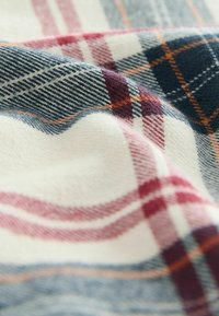 Károvaná tkanina v bielej, námorníckej a červenej farbe má mriežkové vzory s jemnými čiarami. Mäkka textura, mierne krčený vzhľad.