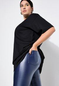 Zwart oversized t-shirt met korte mouwen, gecombineerd met glanzende blauwe faux-lederen broek, met een achterzak en een gladde textuur.