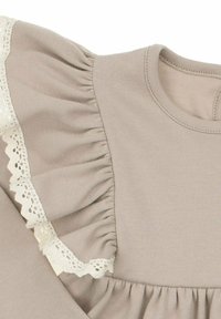 Beżowy top z tkaniny z marszczonymi rękawami ozdobionymi koronką oraz marszczonym przodem, tworzący teksturowany kontrast w stosunku do gładkiego materiału.