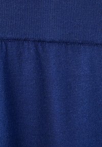 Gros plan d’un tissu tricoté bleu montrant des coutures détaillées et une ligne de couture horizontale au centre.