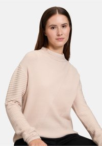 Ljusrosa ribbad tröja med avslappnad passform, med hög hals och texturerade ärmar, tillverkad av ett mjukt tyg.