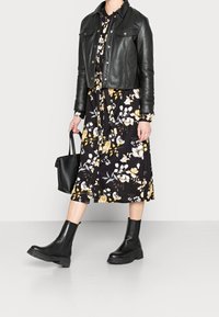 Giubbotto corto in pelle nera, abito midi floreale nero e giallo, borsa nera, e stivaletti neri chunky con suola testurizzata.
