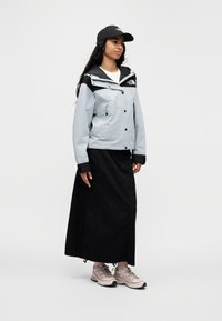 Ανοιχτό μπλε αδιάβροχο μπουφάν με μαύρο κουκούλα και μανσέτες· συνοδεύεται από μαύρη φούστα και αθλητικά παπούτσια ροζ-γκρι. Καπέλο με λογότυπο.