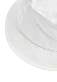 Cappello a secchiello bianco in cotone con una larga visiera inclinata verso il basso. Presenta una sottile texture a righe e cuciture ordinate lungo i bordi.