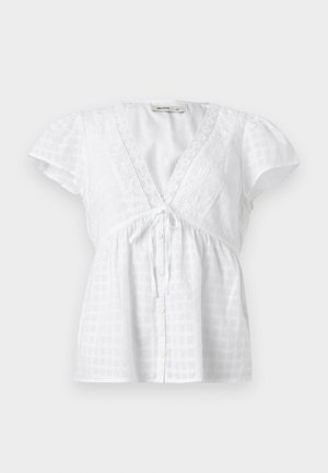 Λευκό μπλουζάκι με κοντό μανίκι, V-λαιμόκοψη με δαντελένιο τελείωμα, κουμπιά μπροστά, δέσιμο κάτω από το στήθος και διακριτικό καρό σχέδιο στο ύφασμα.
