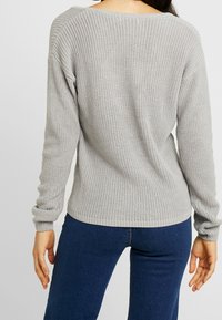 Pull en tricot gris avec une coupe ample, encolure large et poignets côtelés, présentant un tissu texturé et une drapée décontractée à l'arrière.