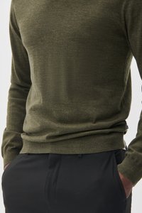 Olivgrön stickad tröja med långa ärmar, rund halsringning och ribbad nederkant. Kombinerad med svarta skräddarsydda byxor. Subtil struktur noteras.