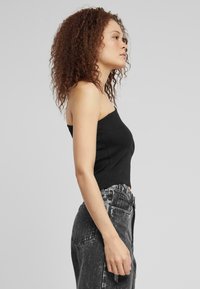 Svart ribbet crop-top kombinert med syrevaskeede høytaljede jeans, med sidelommer og en avslappet passform. Håret stylet i løse krøller.