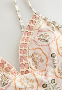 Gros plan sur un tissu à motif floral avec une bordure en crochet rose et crème et des bretelles rayées vertes et blanches sur un fond clair.
