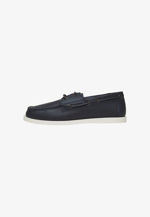 Chaussure bateau en cuir bleu marine avec semelle en caoutchouc blanche, couture moc toe et détail lacets le long des côtés.