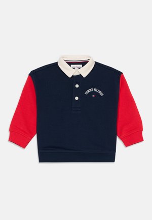 Polo manches longues avec corps bleu marine, manches rouges, col blanc, deux boutons et logo Tommy Hilfiger sur la poitrine.