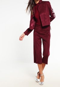 Burgundy mockaskinn tvådelat set med en kort jacka med knapprad och broderade detaljer, som är stiligt kombinerat med vida culottbyxor.