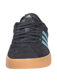 Čierne semišové tenisky s tyrkysovými pruhmi, gumenou podrážkou, okrúhlou špicou a klasickým šnurovaním. Na jazyku sa nachádza logo Adidas.