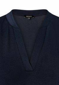 Haut bleu marine avec un design en V, en tissu lisse. Présente un léger éclat et une texture contrastante le long de l'encolure.