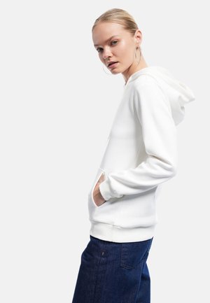 Witte hoodie met een voorzak en geribbelde manchetten, gecombineerd met donkerblauwe spijkerbroeken. Gladde textuur en casual design.