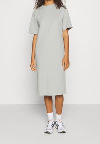 Harmaa puuvillatunika, jossa on lyhyet hihat, suora leikkaus ja polvipituus. Yhdistetty valkoisiin urheilukenkät ja valkoisiin sukkiin.