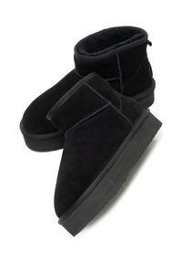 Czarne botki zamszowe z miękkim wnętrzem, płaską gumową podeszwą oraz przeszyciami wzdłuż szwów i wokół otworu buta.