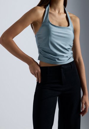 Light blue halter top with a square neckline, ruched texture, and smooth fabric paired with black tailored pants.