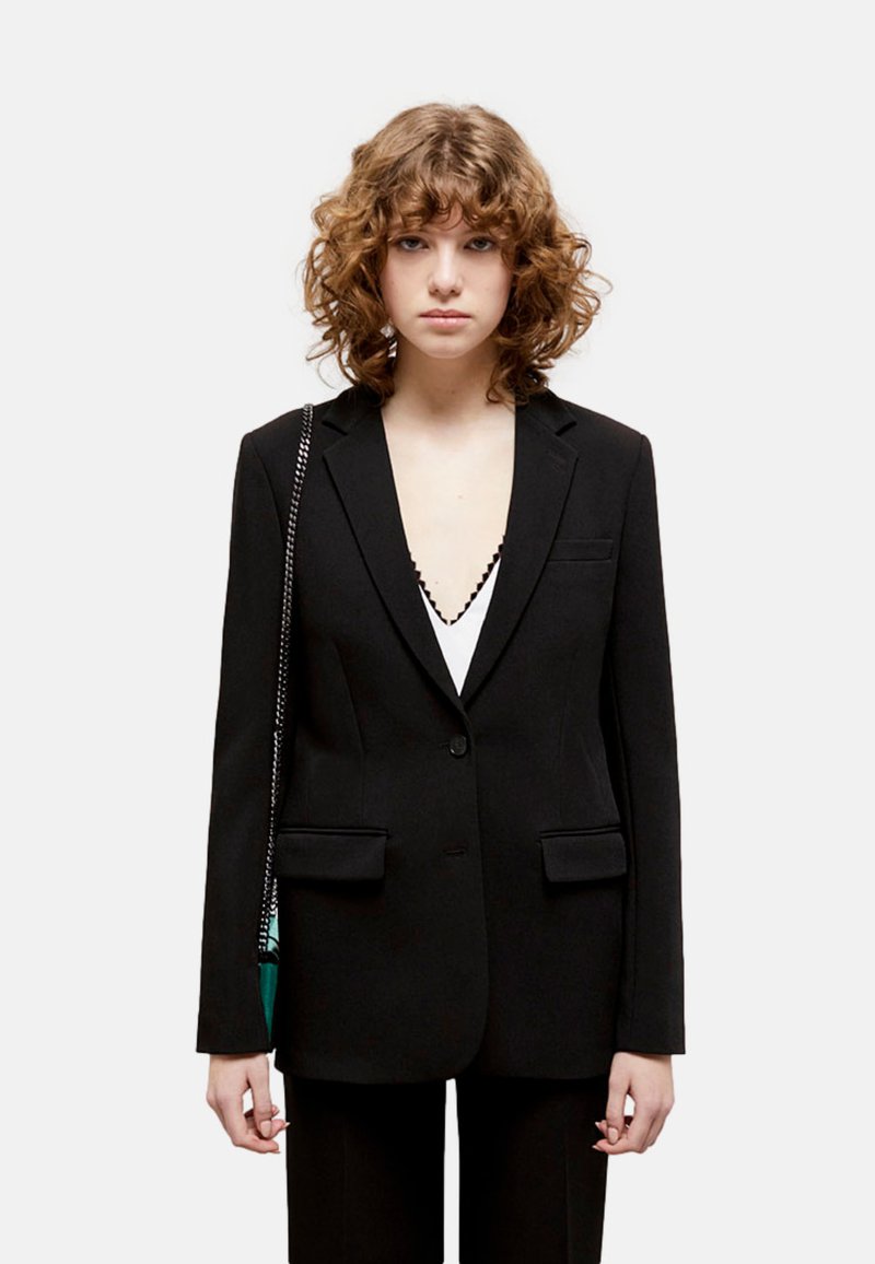 Blazer nero su misura con vestibilità slim, rever a punta, due tasche frontali e chiusura con un bottone. Tessuto morbido e design minimale.