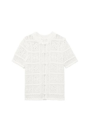Haut blanc en tricot à manches courtes avec un motif ajouré texturé et une fermeture à boutons sur le devant. Ourlet droit et col rond.
