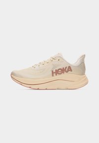 Beige HOKA løpesko med tykk såle, nettmateriale øverst og snøring, vist fra siden mot hvit bakgrunn.