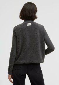 Gray fleece vest with a textured, fluffy surface. Features a tag labeled "SENSES" on the back. Worn over a dark long-sleeve shirt.