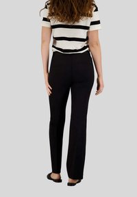 Pantaloni neri aderenti con una texture liscia, abbinati a una maglietta a maniche corte a righe bianche e nere. Presentano una vita e tasche posteriori.